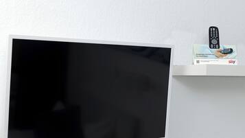 Un televisor de pantalla plana montado en la pared, un control remoto en un estante y una caja con la imagen de un control remoto.