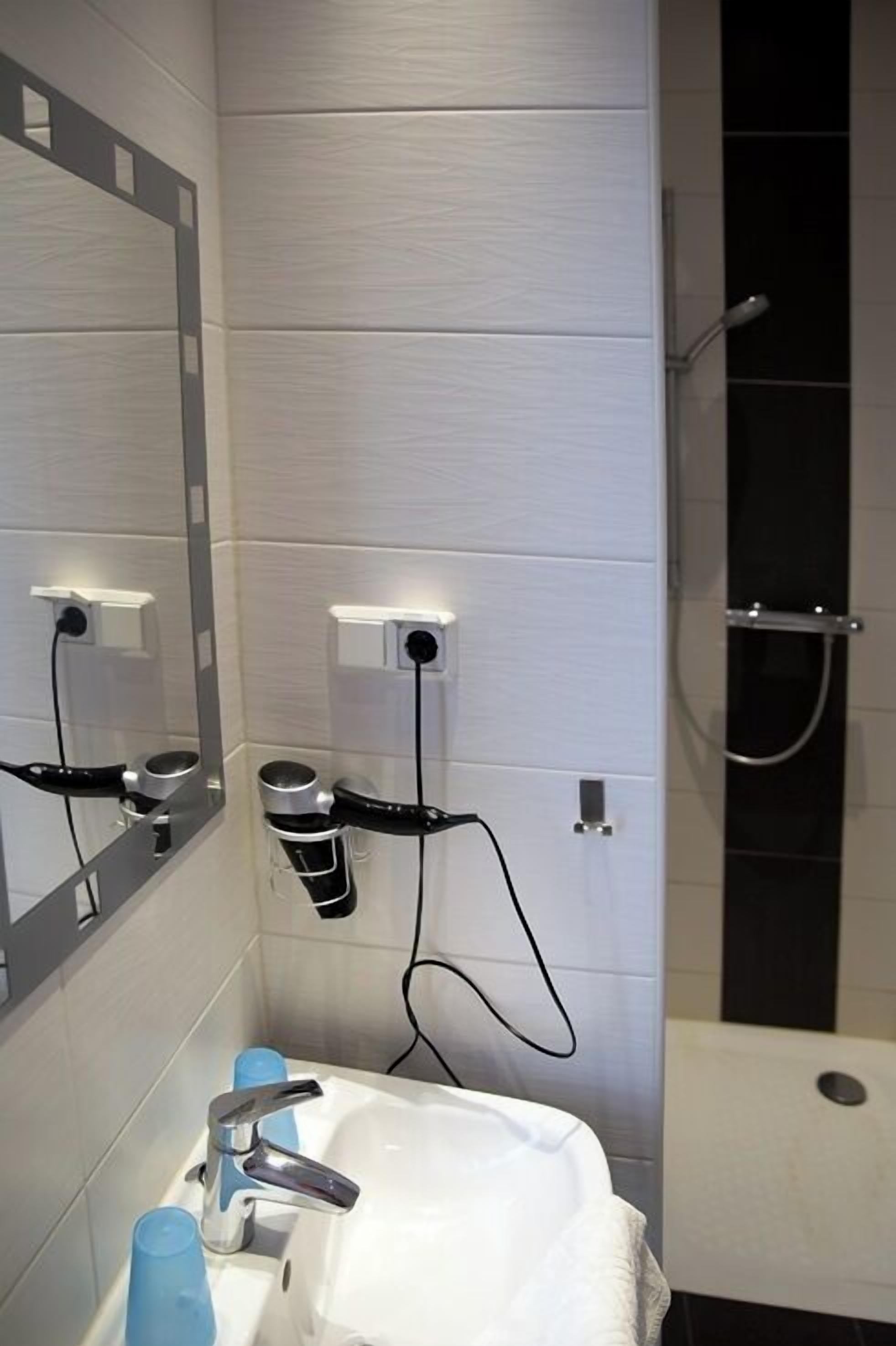 Un baño moderno con un lavamanos blanco, dos secadores de pelo, un espejo y una ducha.