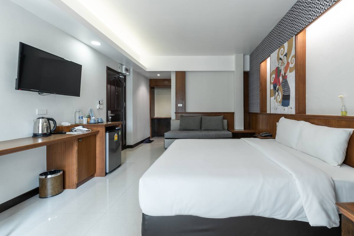A modern hotel room with a large bed, a flat-screen TV, a kitchenette, and a bathroom.