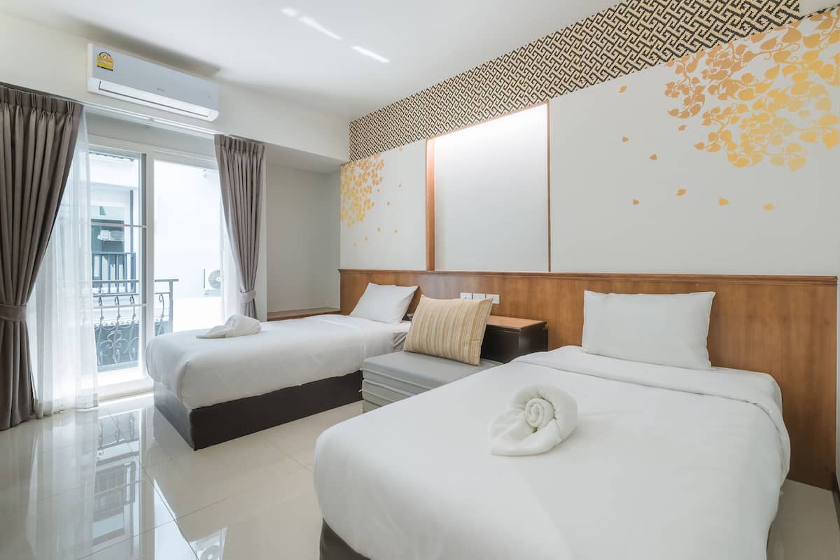 A hotel room with two beds, a wooden headboard, a large window with curtains, and a patterned wall.