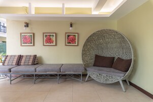 A seating area with a bench and a wicker chair, both with cushions. There are three framed floral paintings on the wall.