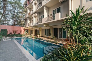 A modern hotel with a swimming pool, balconies, and lush greenery.