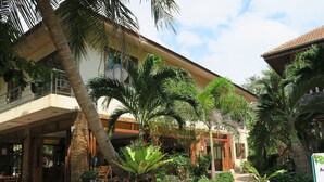 A bungalow-style building with a covered patio, palm trees, and a checkered pathway. - Family House Resort (Ko Pha-ngan)