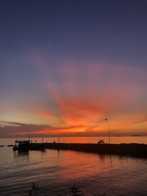 A sunset over a calm body of water with a dock and a street lamp. - Family House Resort (Ko Pha-ngan)
