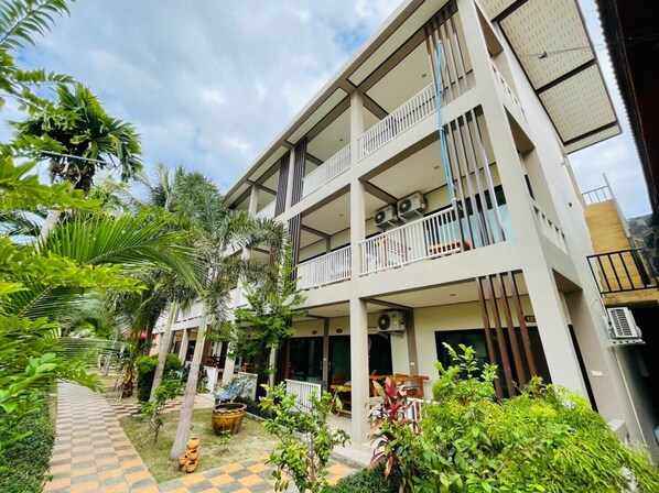A multi-story building with balconies, a checkered pathway, and lush greenery. - Family House Resort (Ko Pha-ngan)