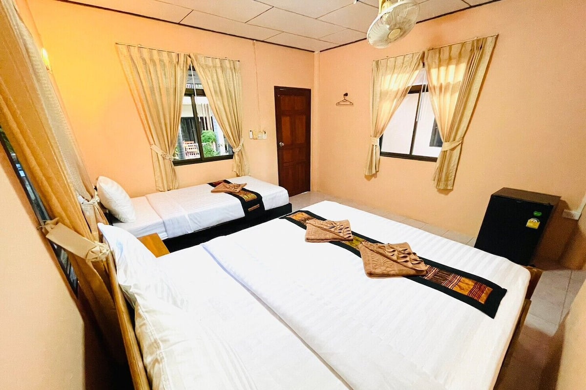 Quarto de hotel com duas camas, uma pequena escrivaninha e um frigorífico.