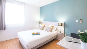 Une chambre d’hôtel avec un lit, une table de chevet avec une lampe, un ordinateur portable et une plante en pot.