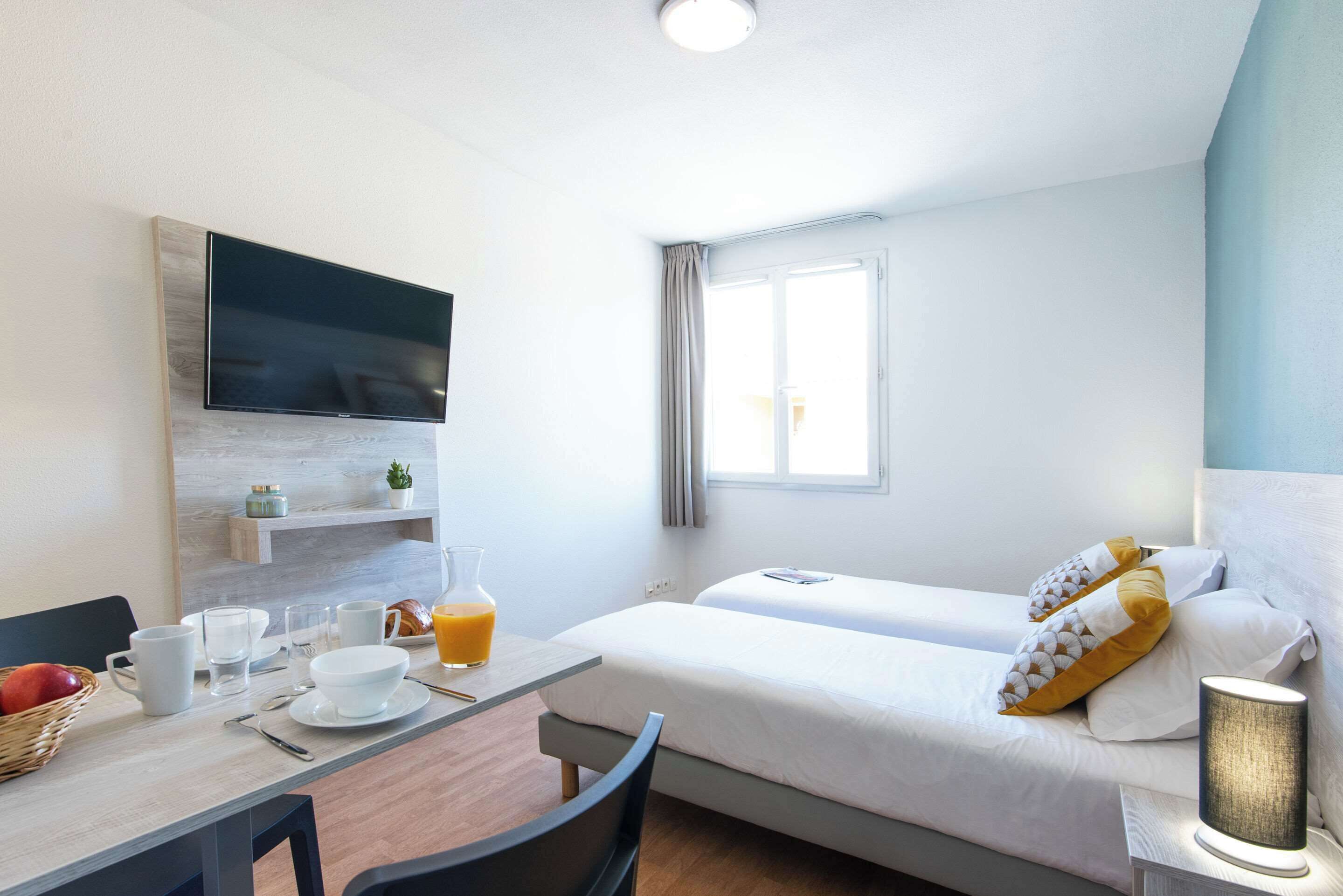 Habitación de hotel con cama, televisor montado en la pared, mesa de desayuno y ventana con cortinas.