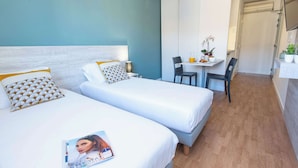 A hotel room with two beds, a small table with chairs, and a bathroom visible in the background. - Comfort Aparthotel Aix Le Tholonet (Le Tholonet)