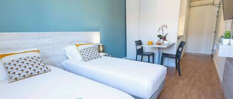 Una habitación de hotel con dos camas, una mesita con sillas y un baño al fondo.