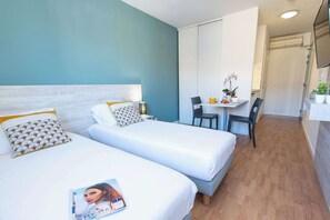 A hotel room with two beds, a small table with chairs, and a bathroom visible in the background.