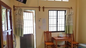 A room with a bed, a wooden table with chairs, a window with bars, and a door with curtains. - Sunny Resort (Phu Quoc)