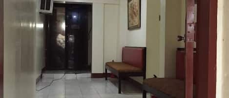A hallway with a tiled floor, a bench, and a door leading to another room.