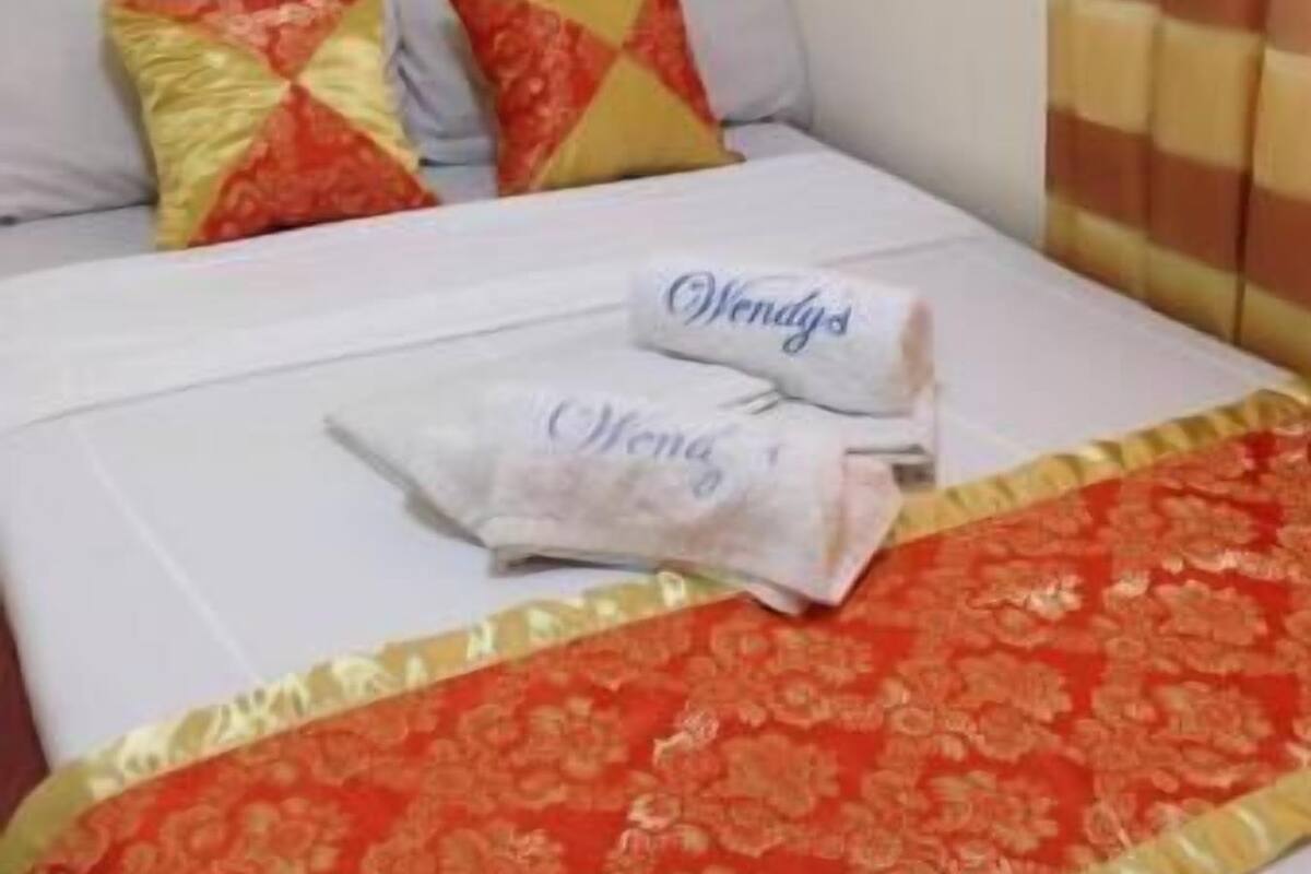 A hotel room with a bed, pillows, a blanket, and a curtain.