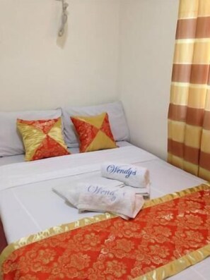 A hotel room with a bed, pillows, a blanket, and a curtain.