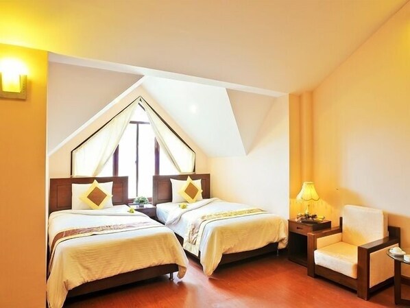 A room with two beds, a chair, a nightstand, and a lamp.