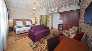 A hotel room with a bed, a purple sofa, a wooden dining table, and a brick wall. - Azade Premier (Istanbul)
