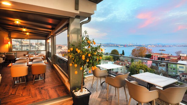 A restaurant with a terrace overlooking a cityscape, featuring wooden flooring, modern furniture, and a potted lemon tree. - Azade Premier (Istanbul)