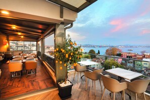 A restaurant with a terrace overlooking a cityscape, featuring wooden flooring, modern furniture, and a potted lemon tree. - Azade Premier (Istanbul)