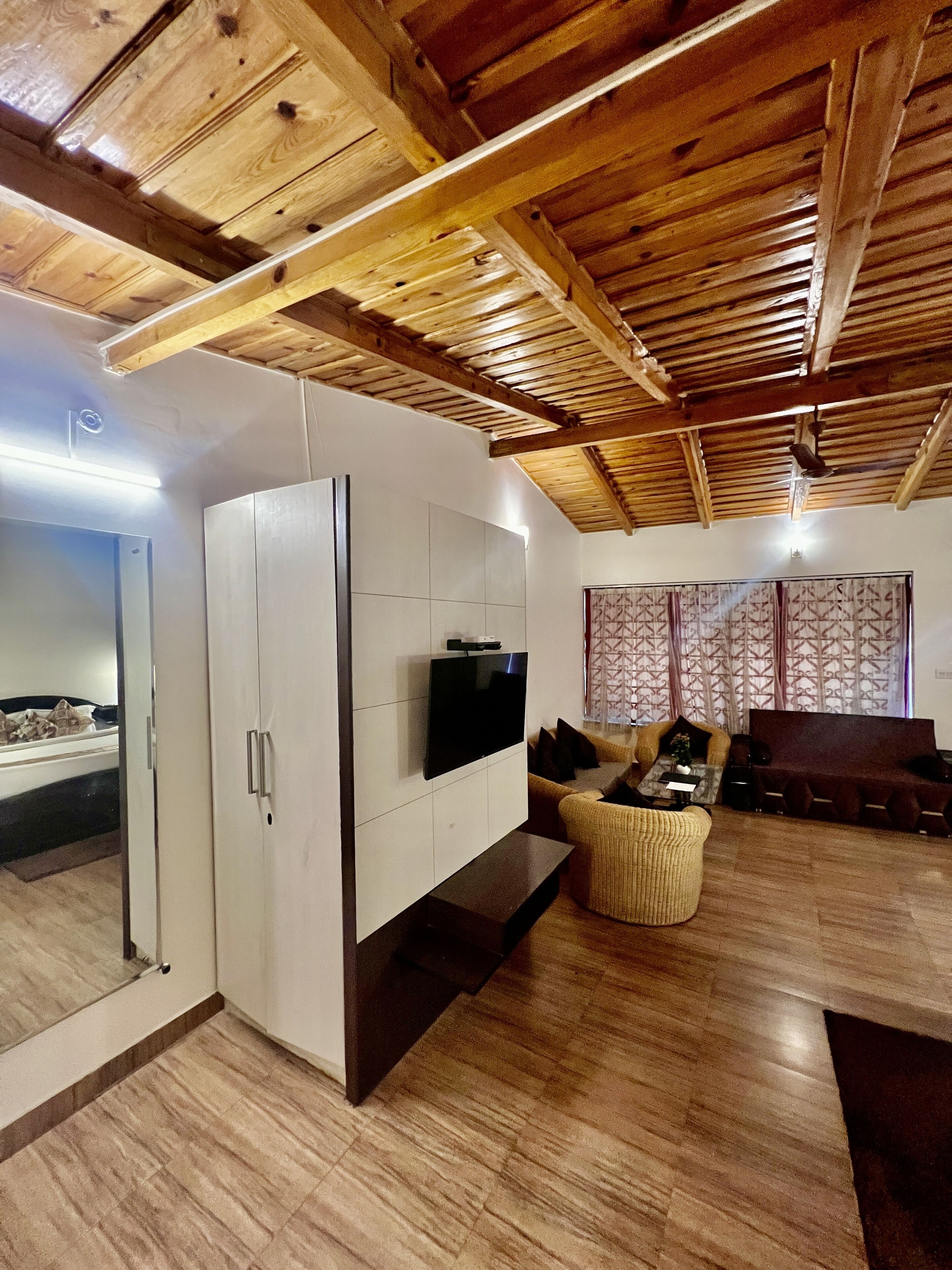 A modern living room with a wooden ceiling, a flat-screen TV mounted on a white cabinet, and a seating area with a sofa and a chair.