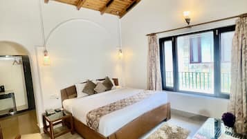 Un dormitorio con techo de madera, una cama con colcha estampada, un escritorio con teclado y una ventana con cortinas.