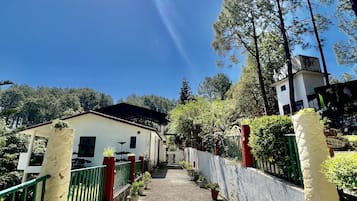 Un sendero que lleva a un edificio con fachada blanca y tejado rojo, rodeado de follaje y árboles.