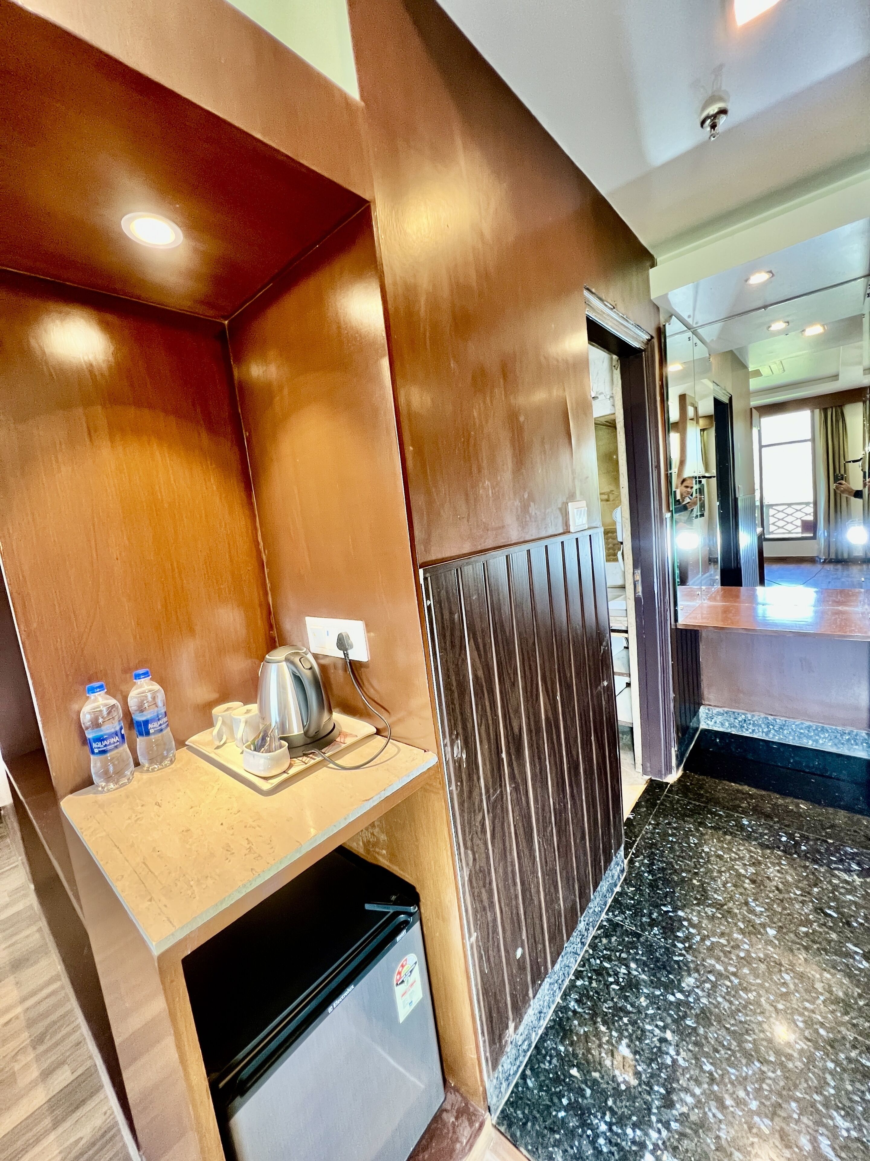 Habitació d'hotel amb nevera petita, mini bar, cafetera i dues ampolles d'aigua.