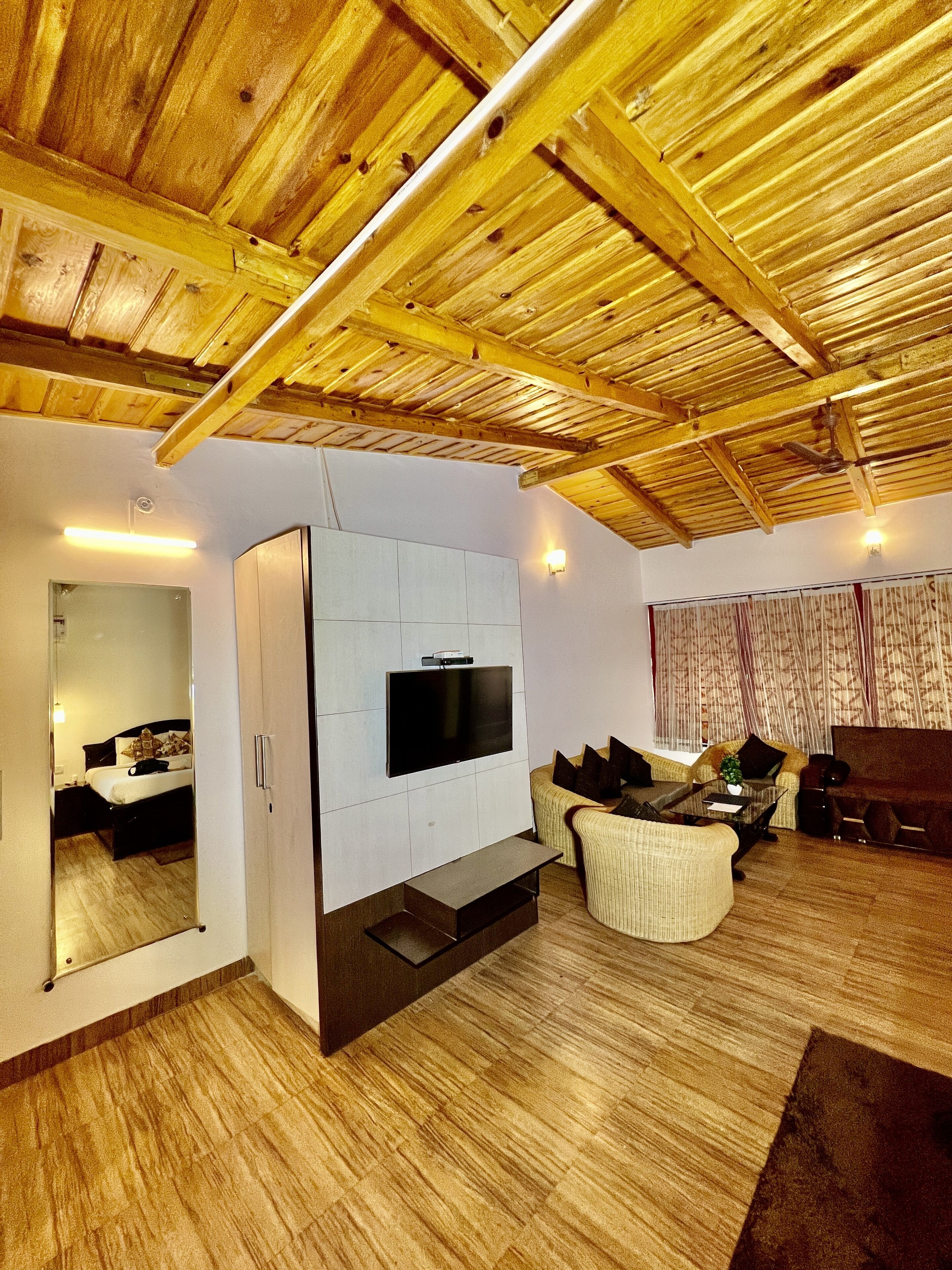A spacious living area with a wooden ceiling, a flat-screen TV mounted on a white cabinet, and a seating area with a sofa and armchairs.