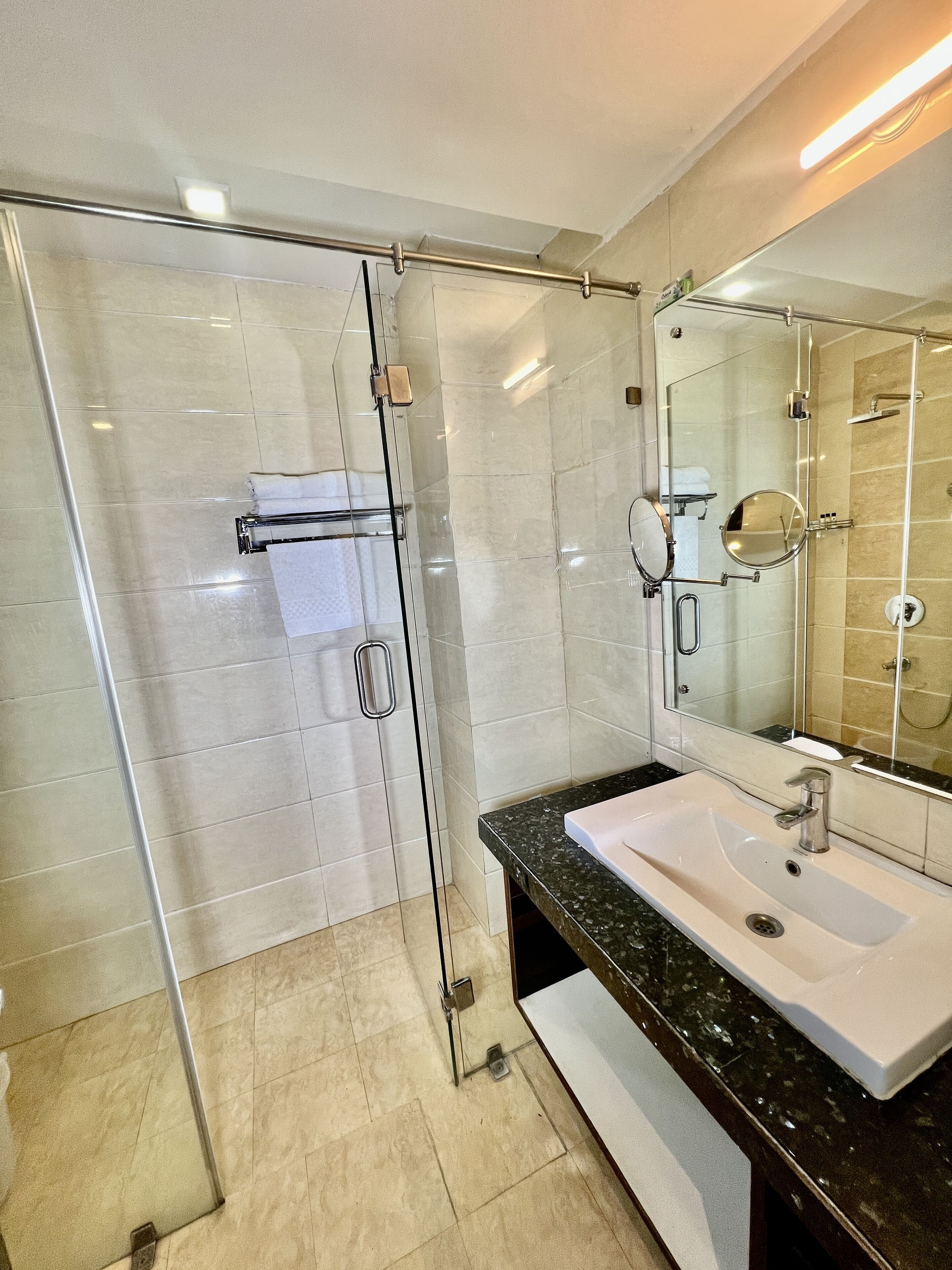 Un baño moderno con ducha de vidrio, un lavabo blanco y un espejo grande.
