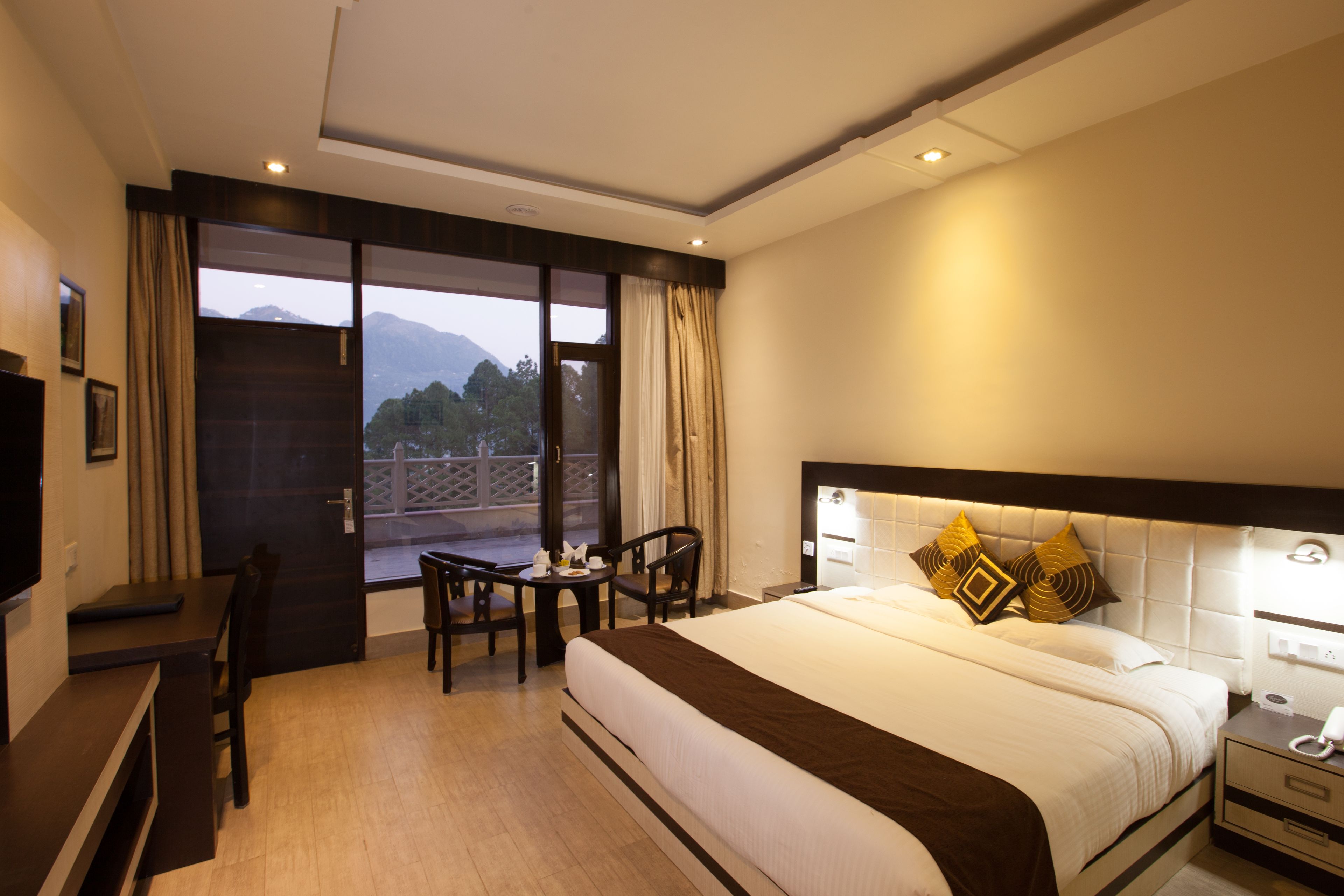 A hotel room with a large bed, a desk, and a chair. There is a window with a view of mountains.