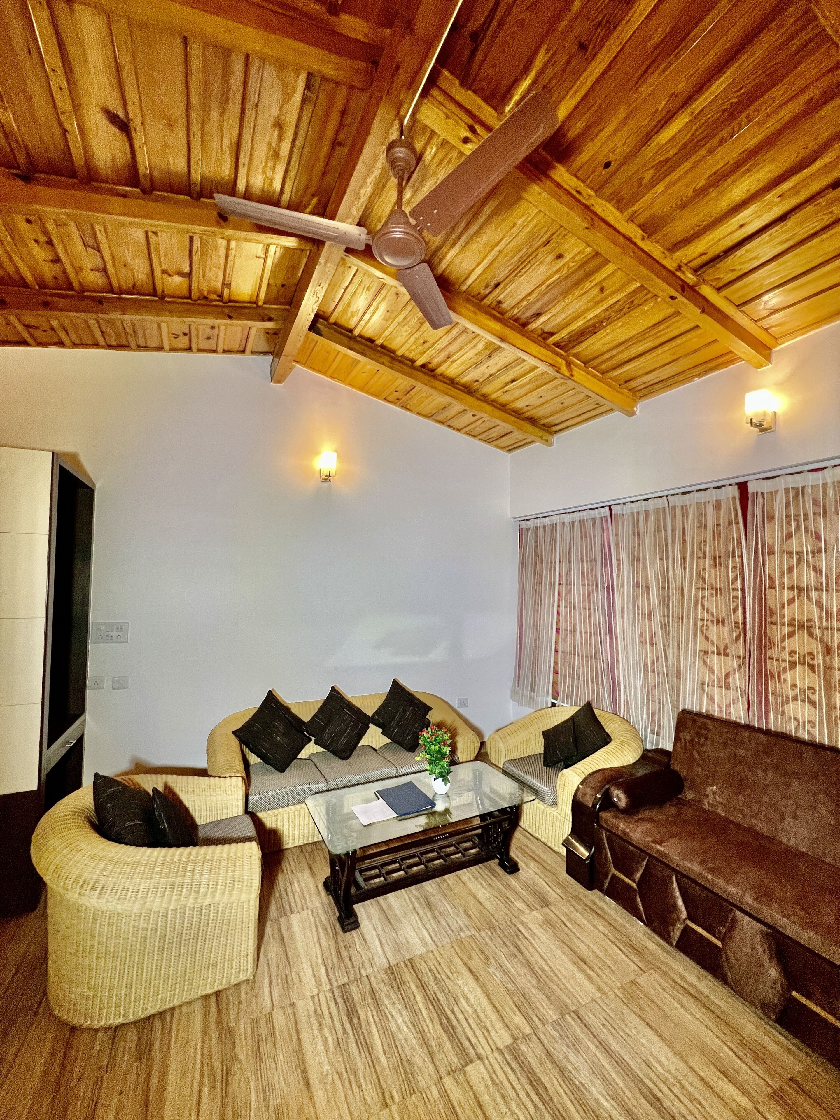 Uma sala de estar com teto de madeira, mesa de centro de vidro, sofá e televisão.