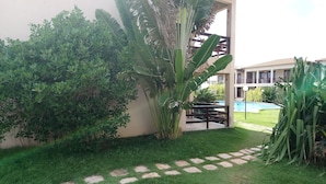 Un jardin bien entretenu, avec un chemin pavé, une végétation luxuriante et une piscine à l’arrière-plan.