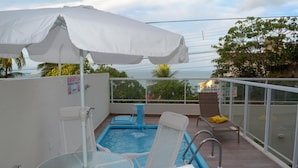 Un espace piscine aménagé sur le toit, avec une table en verre, des chaises longues et un parasol blanc.