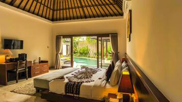 A bedroom with a large bed, a desk, a chair, a TV, and a view of a pool and greenery.