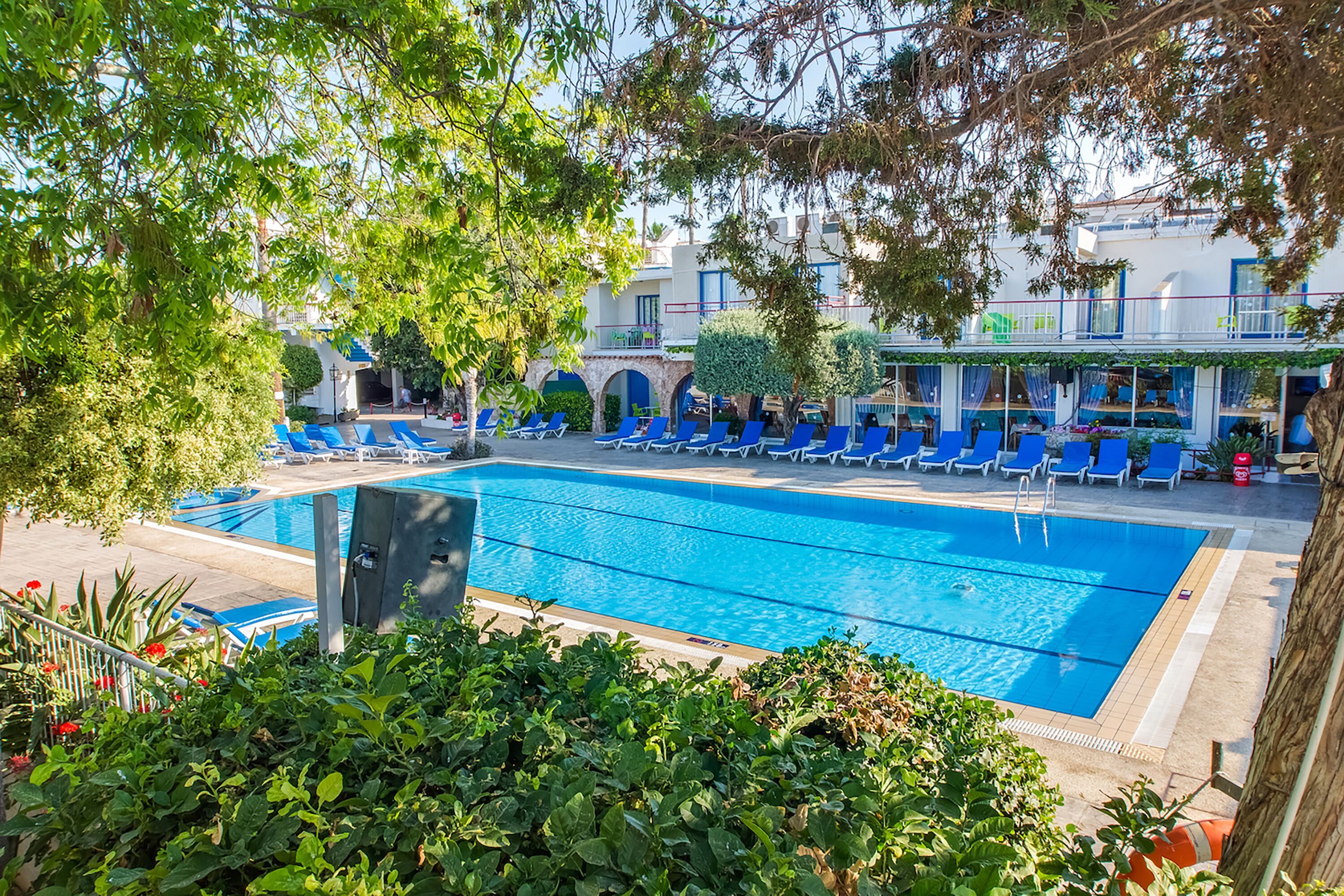 A swimming pool with blue lounge chairs, surrounded by greenery and a building with balconies.
