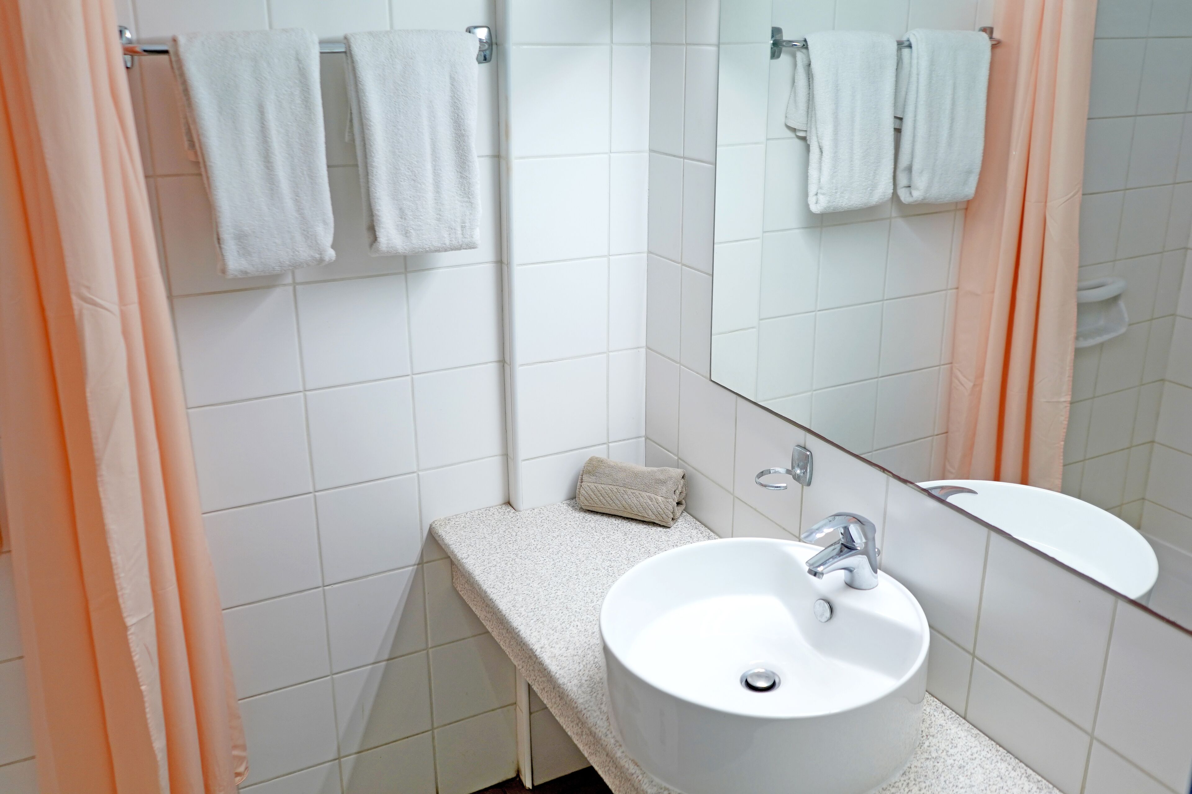 Un baño con un lavamanos blanco, un espejo y un perchero para toallas.