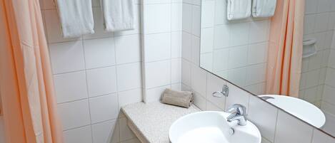 Un baño con un lavamanos blanco, un espejo y un perchero para toallas.