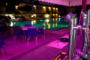 Zona junto a la piscina con bar, sillas y mesa.