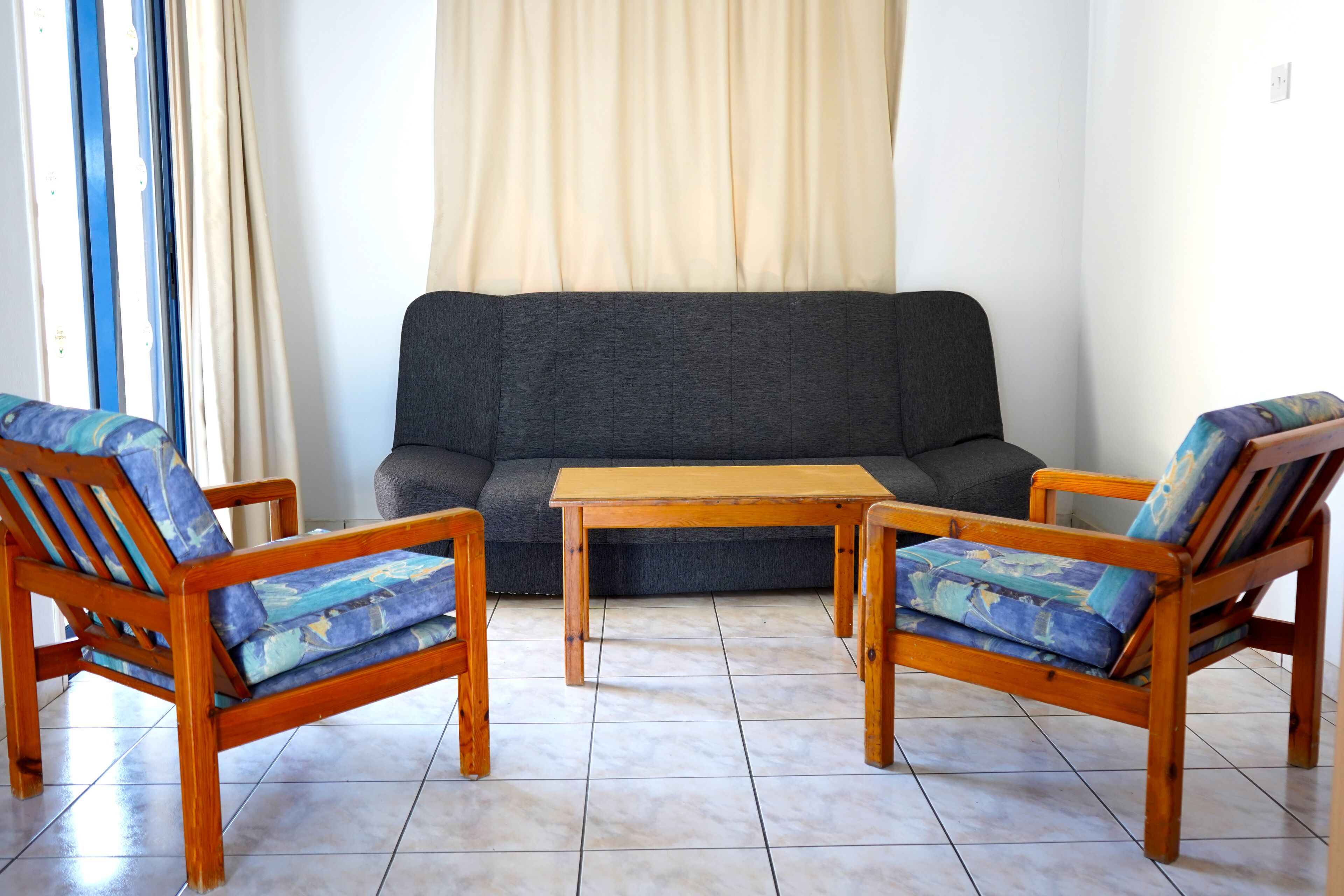 Una sala de estar con un sofá, dos sillas de madera con cojines azules y una mesa de centro de madera.
