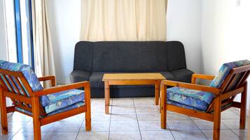 Una sala de estar con un sofá, dos sillas de madera con cojines azules y una mesa de centro de madera.