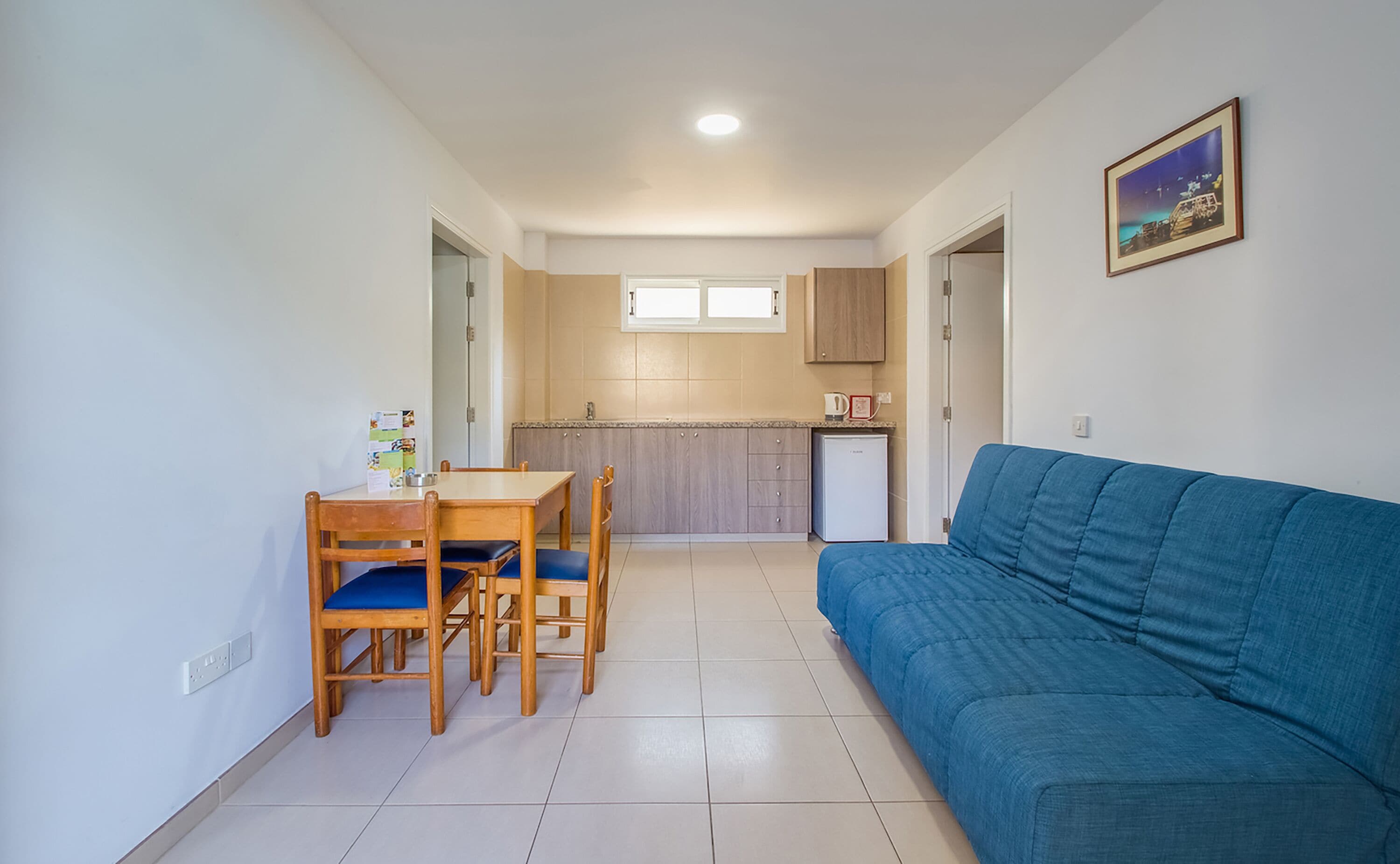 Un espace de vie compact comprenant un coin repas, une kitchenette et un canapé bleu.