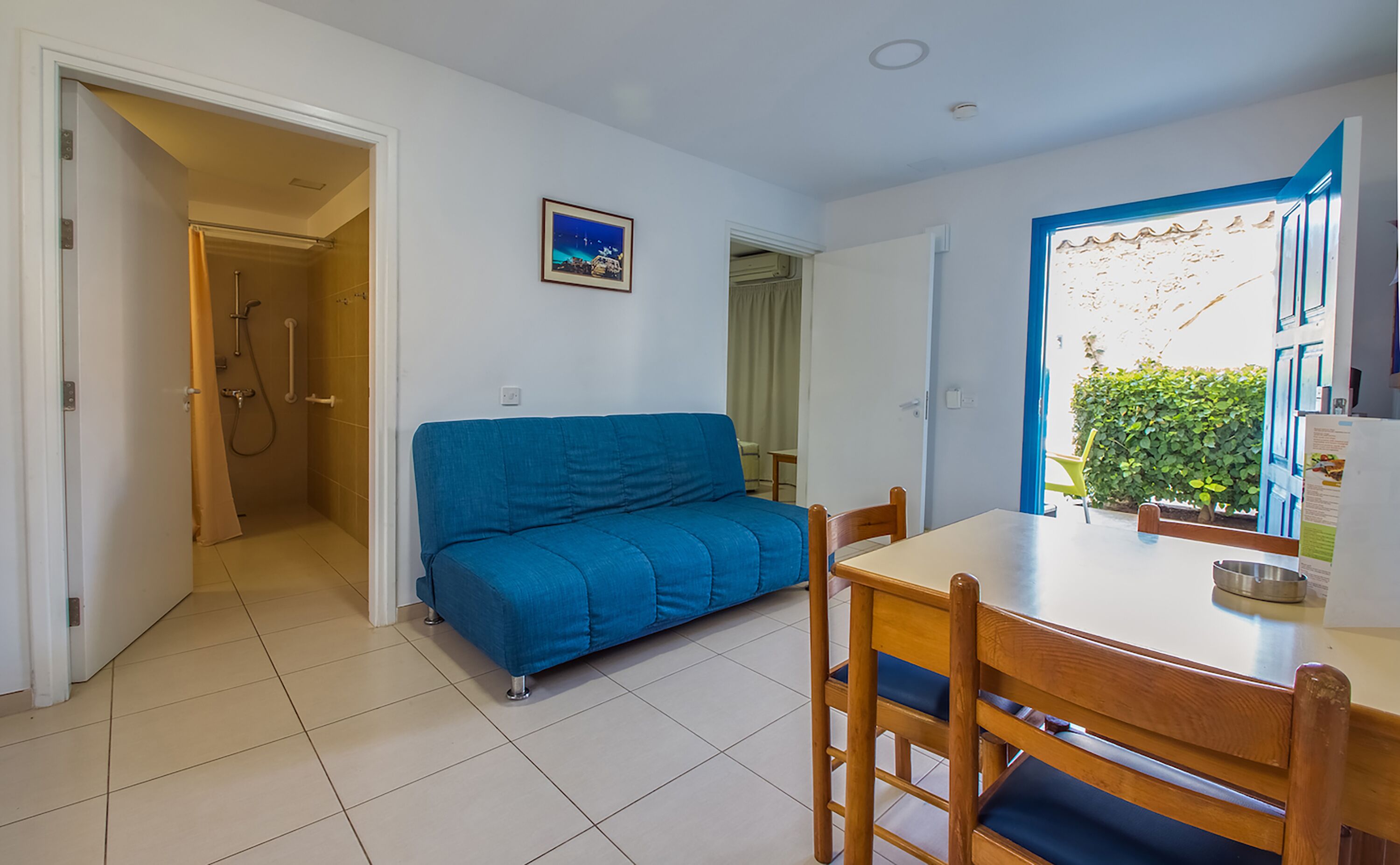 Un espace de vie compact comprenant un canapé bleu, une table à manger avec des chaises et un petit coin cuisine.