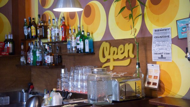 A bar area with a 'OPEN' sign, various liquor bottles, glasses, and a water dispenser.