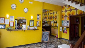 A reception area with a yellow wall, clocks, a Coca-Cola sign, and a staircase.