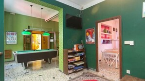 A room with a pool table, a bookshelf, a television, and a door leading to another room.
