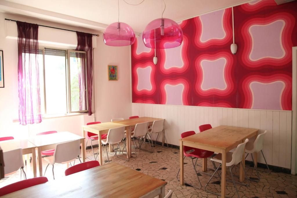 Quarto com mesas, cadeiras, janela com cortinas e parede com padrão geométrico.