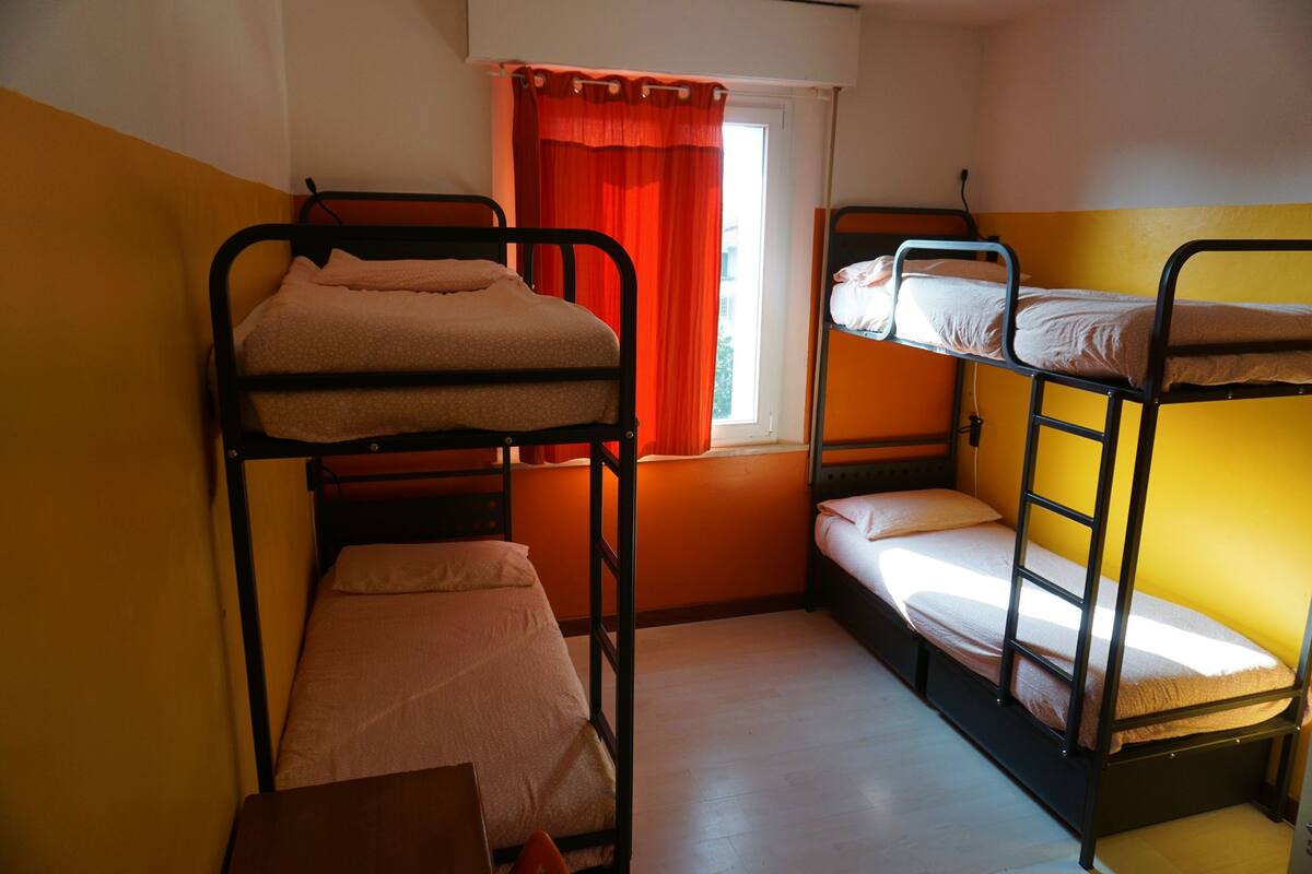Un dormitorio con literas, una ventana con cortinas rojas y una mesita.