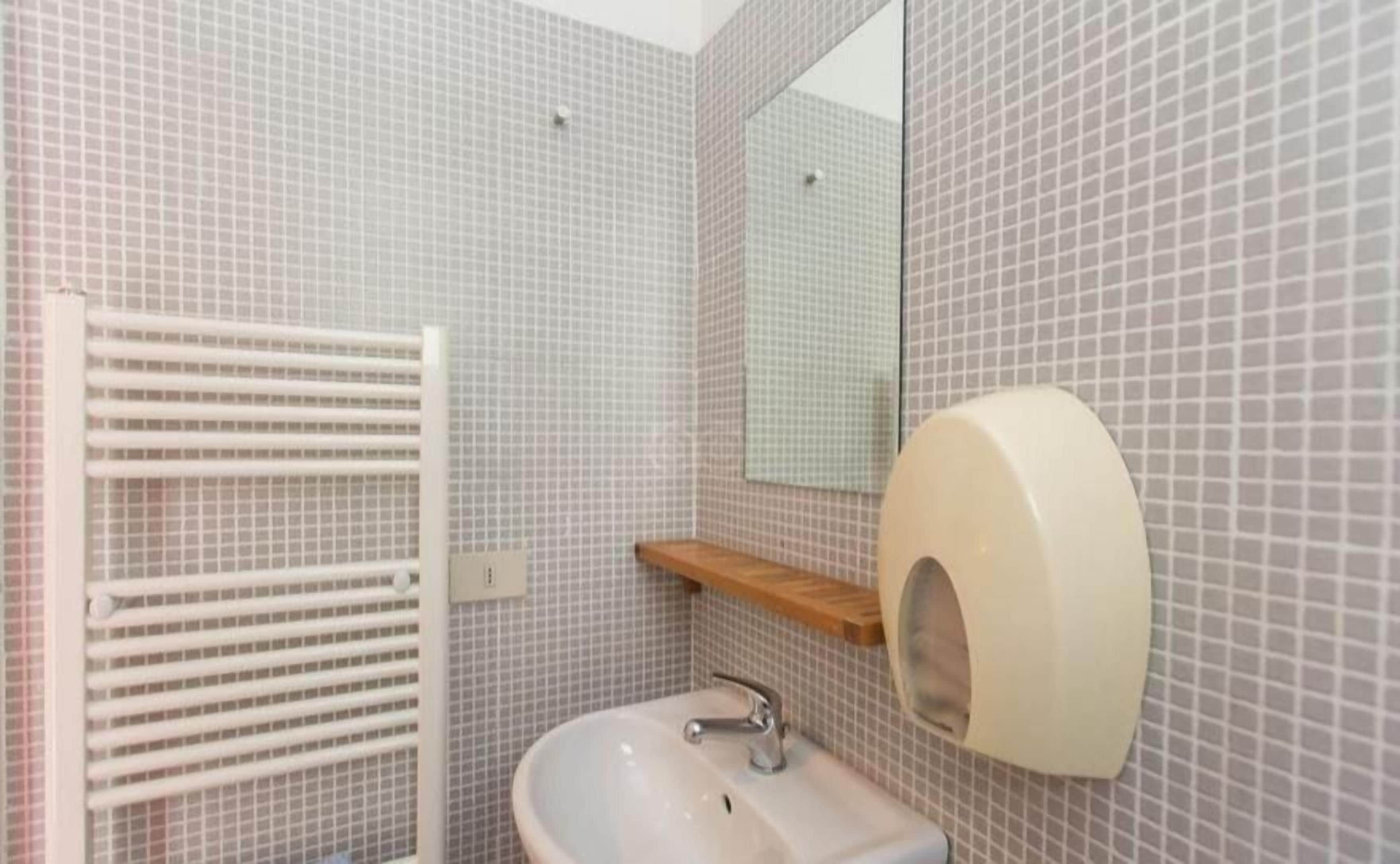 Une salle de bain avec un mur carrelé, un lavabo, un miroir, un distributeur de serviettes et un porte-serviettes.