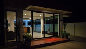A modern house with large glass doors leading to a well-lit interior. - Tikky Place (Chiang Mai)