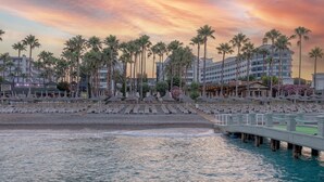 A beachfront hotel with rows of palm trees, a beach with sun loungers, and a bridge over the water. - Meryan Hotel - All Inclusive (Alanya)